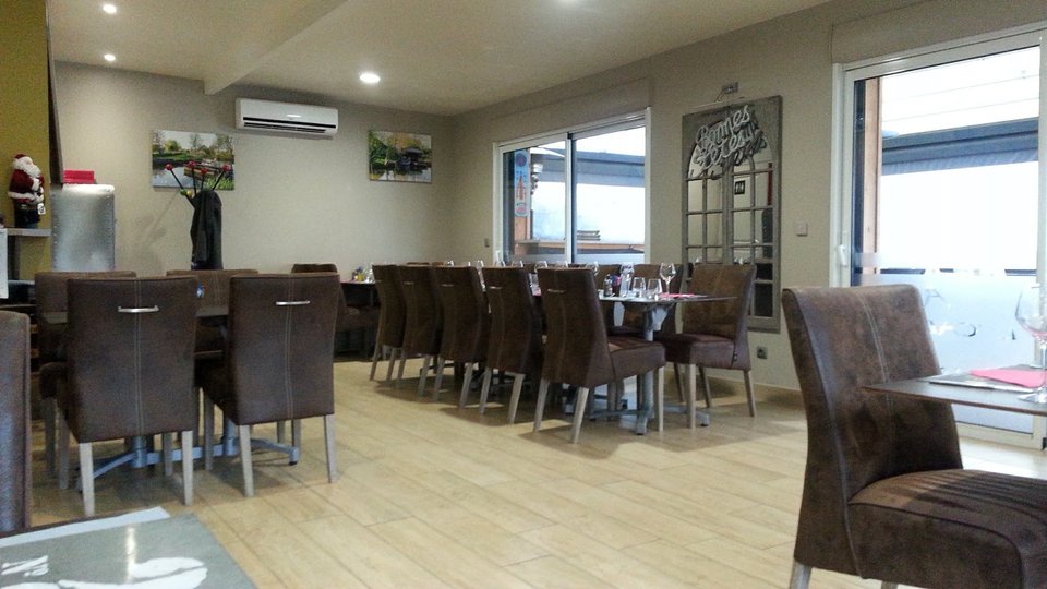 Salle de brasserie avec tables dressées et lumière naturelle.